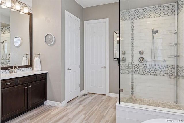 full bath featuring visible vents, vanity, wood finished floors, baseboards, and a stall shower