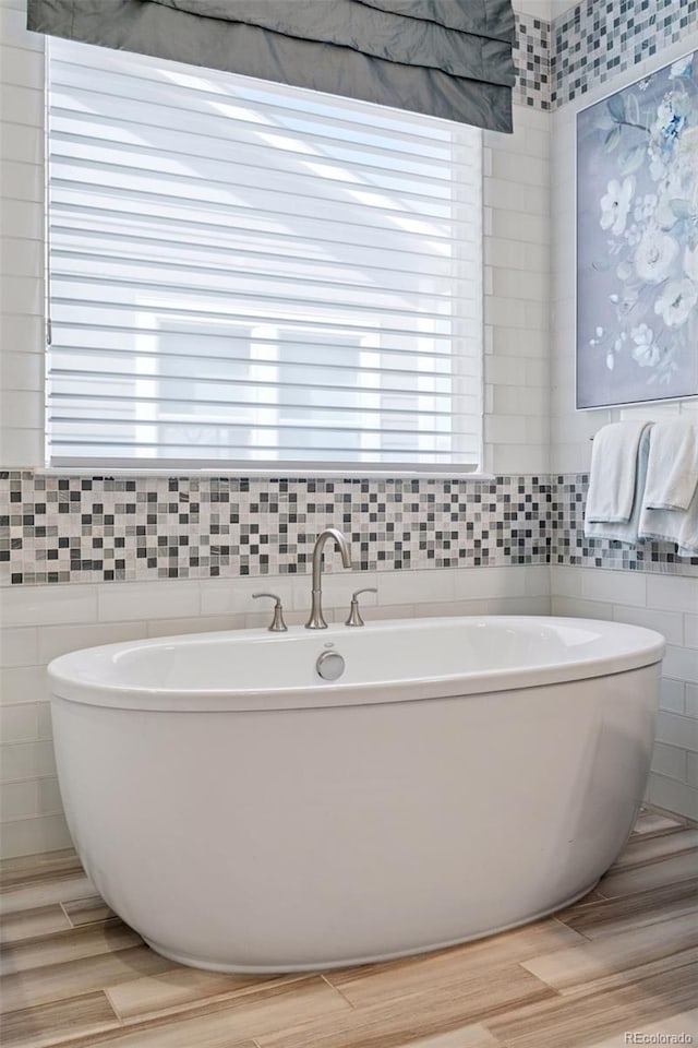 bathroom with wood finished floors, a soaking tub, and tile walls