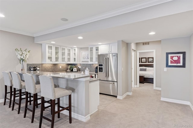 kitchen featuring visible vents, a peninsula, a kitchen bar, and stainless steel fridge with ice dispenser