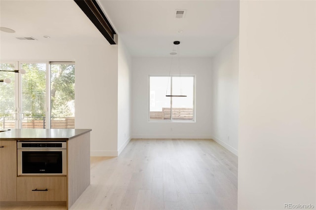 interior space with hanging light fixtures, light brown cabinetry, oven, and light hardwood / wood-style floors