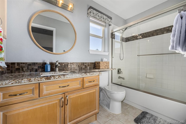 full bathroom featuring tile patterned flooring, backsplash, bath / shower combo with glass door, toilet, and vanity