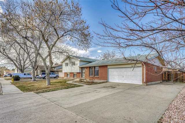 tri-level home with driveway, fence, a shingled roof, a garage, and brick siding