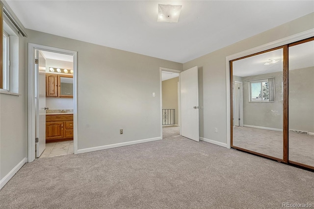 unfurnished bedroom featuring a closet, baseboards, light colored carpet, and ensuite bath