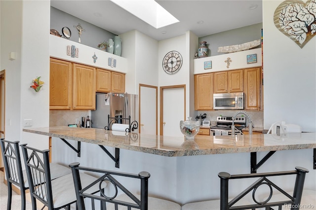 kitchen with a skylight, backsplash, stainless steel appliances, kitchen peninsula, and a kitchen breakfast bar