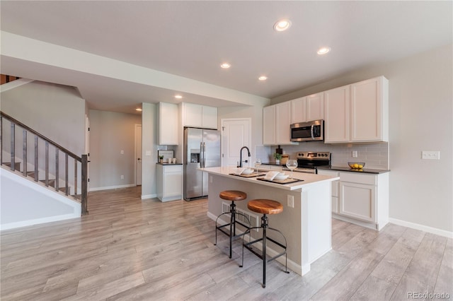 2640 Brookstone Dr Unit B, Milliken, CO 80543 - kitchen with appliances with stainless steel finishes, light wood-style floors, a kitchen island with sink, tasteful backsplash, and a breakfast bar area