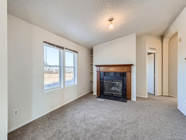 unfurnished living room with a tiled fireplace, carpet flooring, and a textured ceiling