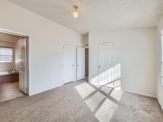 unfurnished bedroom with ensuite bathroom, a textured ceiling, light carpet, two closets, and vaulted ceiling