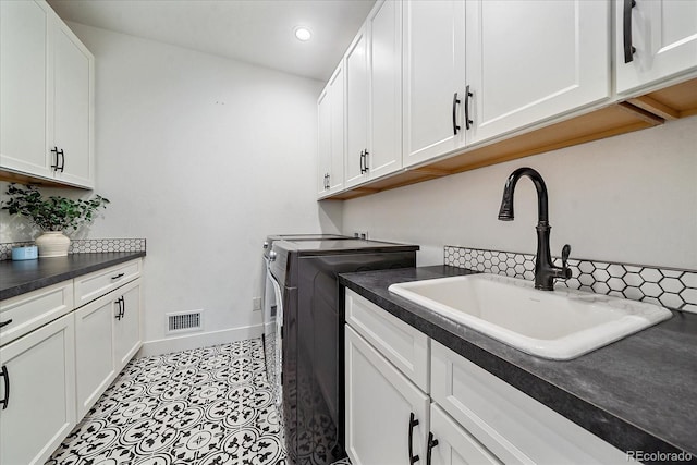 clothes washing area featuring sink, washing machine and clothes dryer, and cabinets