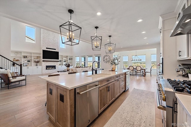 kitchen with hanging light fixtures, range hood, a center island with sink, sink, and white cabinetry