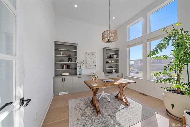 office area with a towering ceiling, a chandelier, light wood-type flooring, and a wealth of natural light