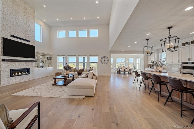 living room featuring light hardwood / wood-style floors, a stone fireplace, and a towering ceiling