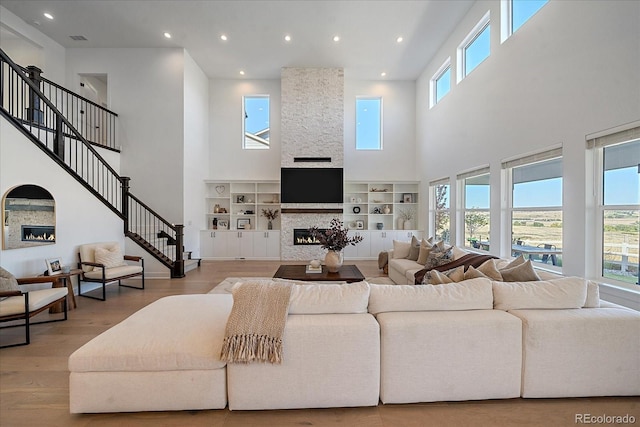 living room with light hardwood / wood-style floors, a stone fireplace, and a high ceiling