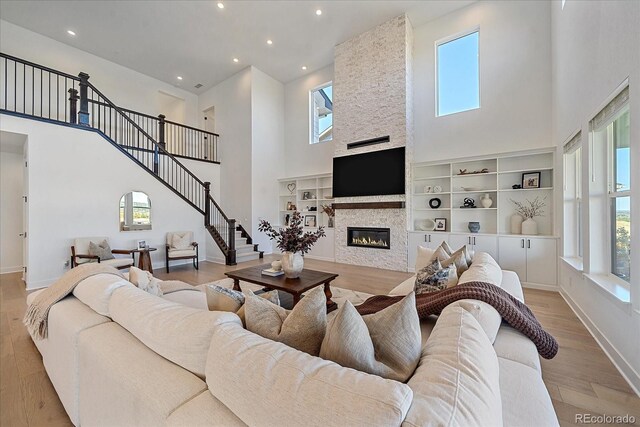 living room with a high ceiling, a stone fireplace, built in shelves, and light hardwood / wood-style floors