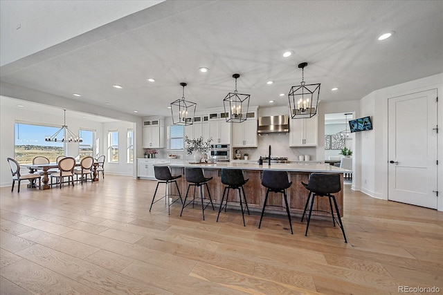 kitchen with white cabinets, light wood-type flooring, pendant lighting, and a kitchen breakfast bar