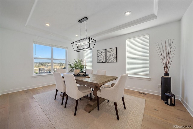 dining area with a notable chandelier, light hardwood / wood-style floors, a tray ceiling, and a wealth of natural light