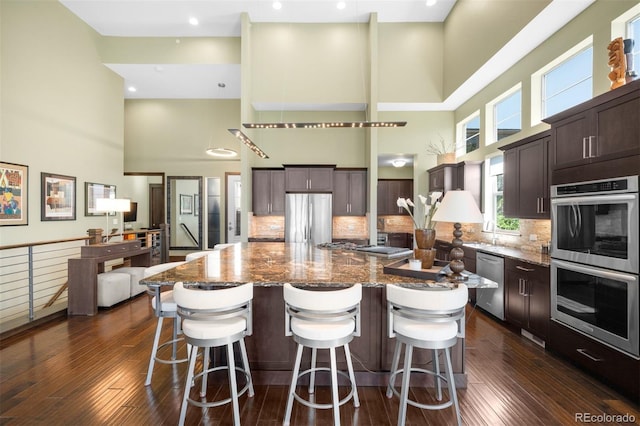 10243 Spring Green Dr, Englewood, CO 80112 - kitchen featuring appliances with stainless steel finishes, a towering ceiling, dark brown cabinets, a spacious island, and dark stone countertops