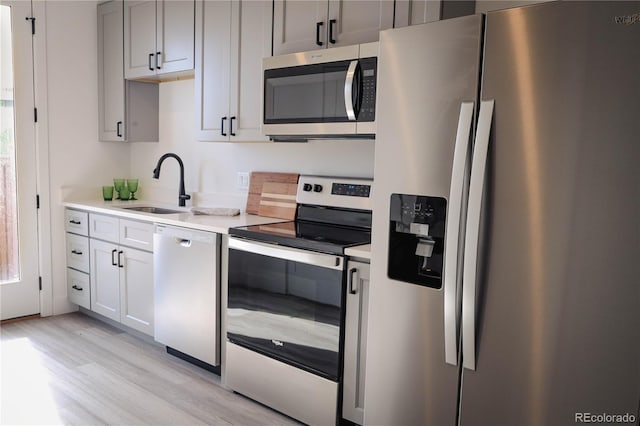 kitchen with appliances with stainless steel finishes, light countertops, a sink, and light wood-style flooring