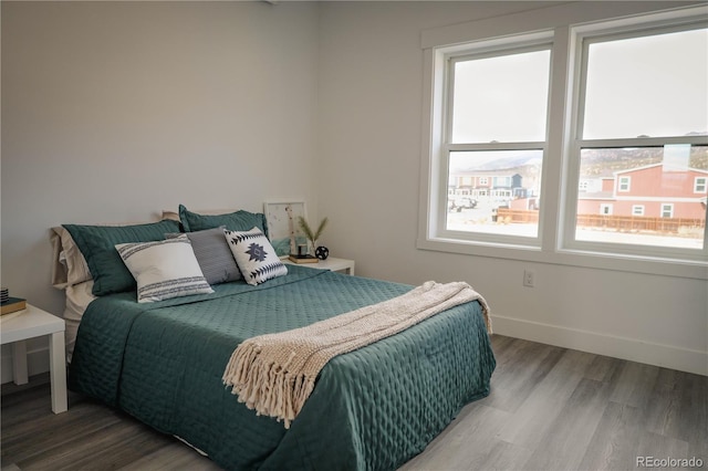 bedroom with multiple windows, wood finished floors, and baseboards