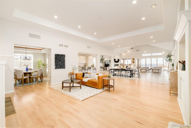 living room featuring a notable chandelier, a tray ceiling, a high ceiling, and light wood-type flooring