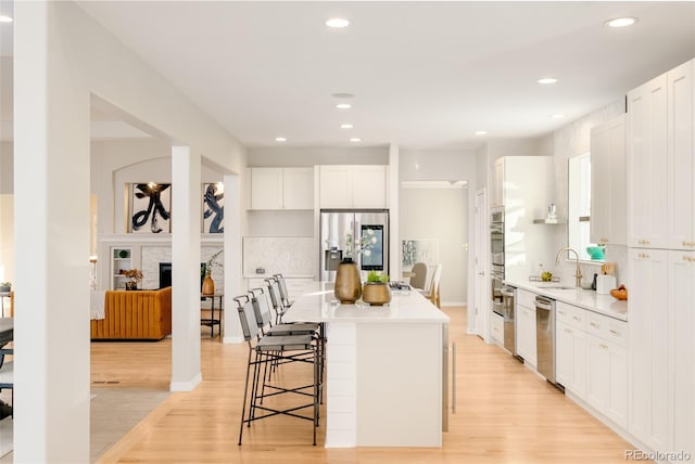 kitchen with a kitchen bar, white cabinetry, stainless steel fridge with ice dispenser, a kitchen island, and light hardwood / wood-style floors