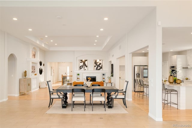 dining space with a brick fireplace, a tray ceiling, built in features, and light hardwood / wood-style floors