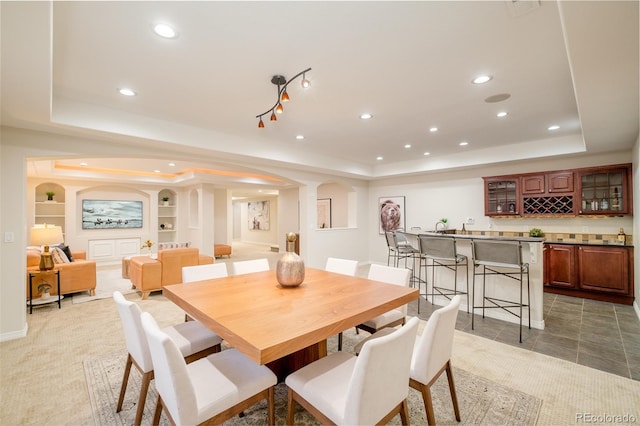 dining space featuring built in shelves, tile patterned floors, a raised ceiling, and indoor bar