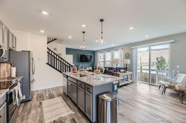 kitchen with a kitchen island with sink, hardwood / wood-style flooring, sink, light stone countertops, and decorative light fixtures