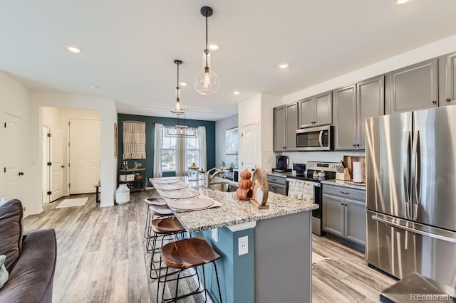 kitchen with appliances with stainless steel finishes, gray cabinets, pendant lighting, and a kitchen island with sink