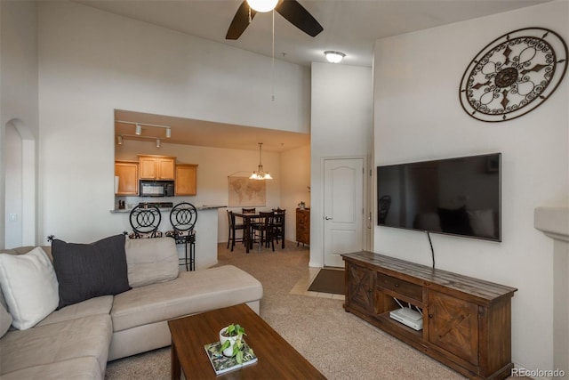 living room with a high ceiling, ceiling fan with notable chandelier, and light carpet