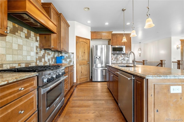 1195 W 70th Ave, Denver, CO 80221 - kitchen featuring stainless steel appliances, custom range hood, an island with sink, light wood finished floors, and light stone countertops