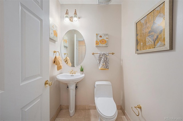 half bath with tile patterned flooring, baseboards, a sink, and toilet