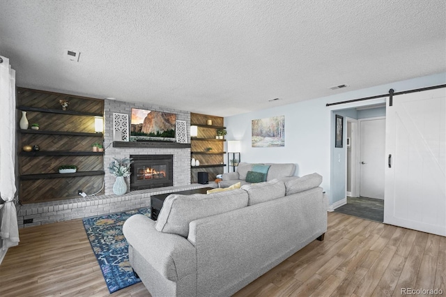8815 W Quarto Cir, Littleton, CO 80128 - living room with a barn door, a textured ceiling, wood finished floors, a brick fireplace, and baseboards