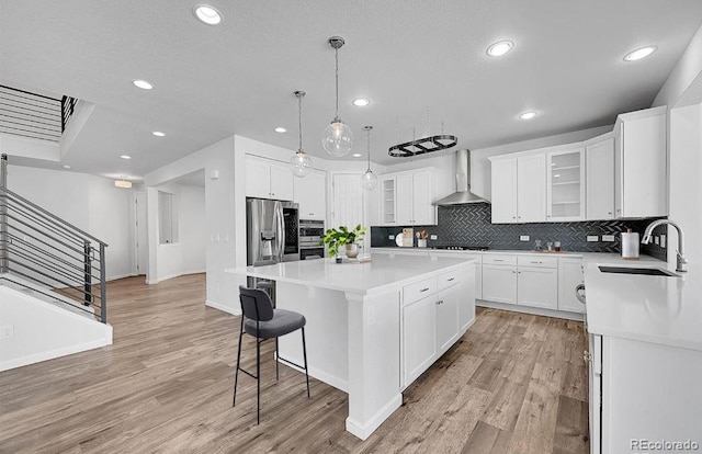 kitchen with white cabinetry, wall chimney exhaust hood, sink, and a kitchen island