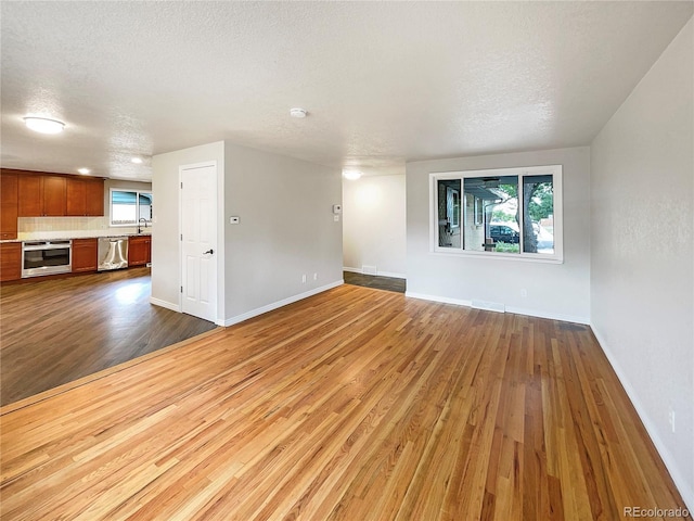 unfurnished living room with visible vents, a sink, a textured ceiling, dark wood finished floors, and baseboards