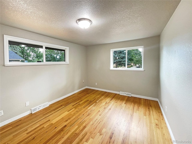 empty room with a textured ceiling, light hardwood / wood-style floors, and a healthy amount of sunlight