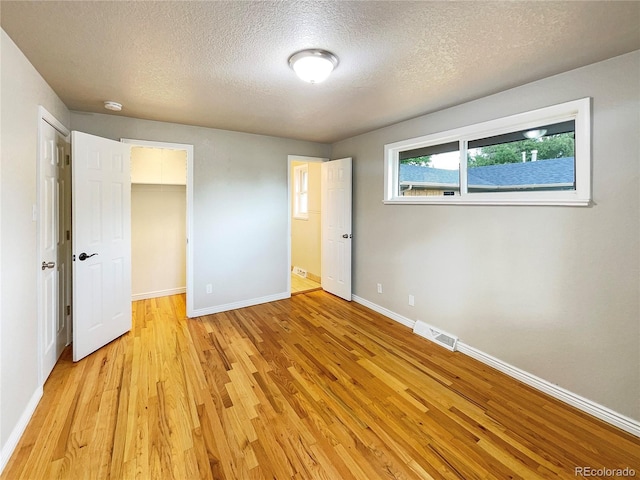 unfurnished bedroom with a spacious closet, a closet, a textured ceiling, and light wood-type flooring