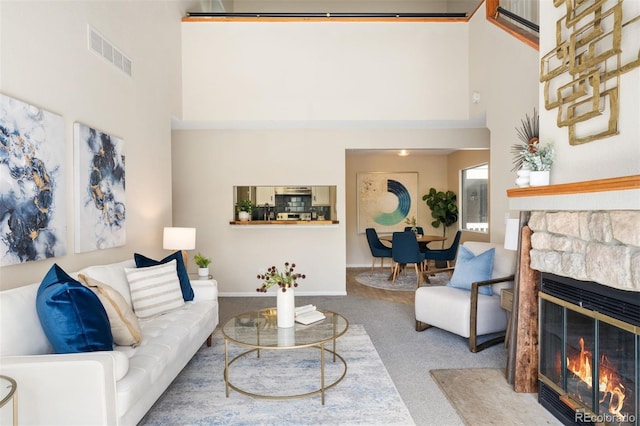 living room with a towering ceiling, a fireplace, and carpet floors