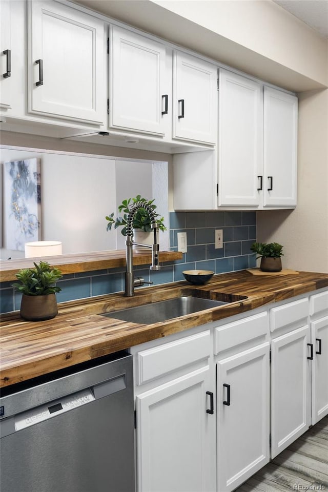 kitchen featuring wooden counters, dishwasher, a sink, white cabinetry, and tasteful backsplash