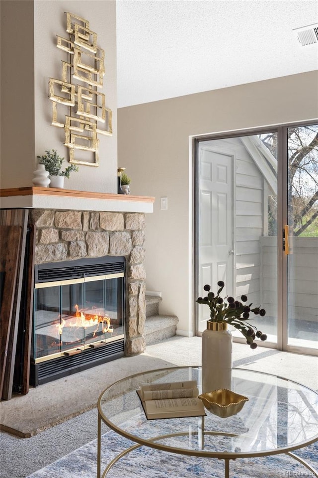 carpeted living area with a stone fireplace and stairs