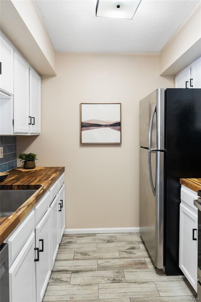 kitchen with wood counters, freestanding refrigerator, wood finish floors, and white cabinetry