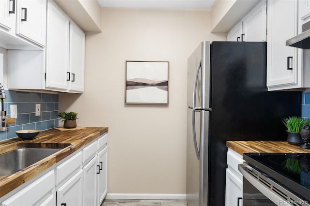 kitchen with butcher block counters, tasteful backsplash, white cabinetry, and wall chimney range hood