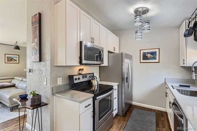 4063 S Quintero Way, Aurora, CO 80013 - kitchen featuring appliances with stainless steel finishes, dark wood-style flooring, a textured ceiling, white cabinets, and baseboards