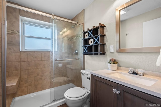 bathroom with toilet, vanity, a textured wall, and a shower stall