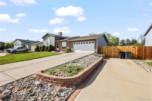 tri-level home featuring concrete driveway, a front lawn, an attached garage, and fence