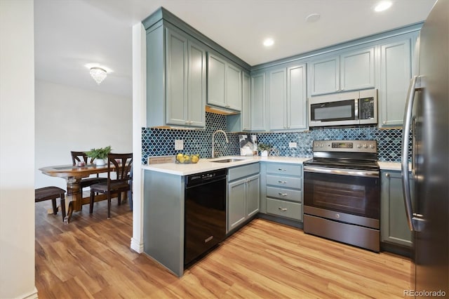 kitchen featuring light wood finished floors, stainless steel appliances, light countertops, a sink, and decorative backsplash