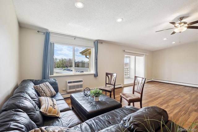 living area featuring a wall mounted air conditioner, baseboard heating, wood finished floors, a textured ceiling, and ceiling fan