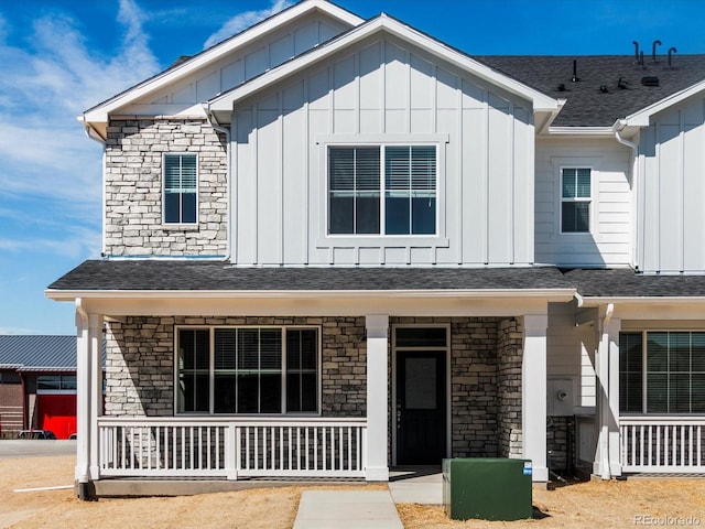 view of front of house featuring board and batten siding, a shingled roof, covered porch, and stone siding