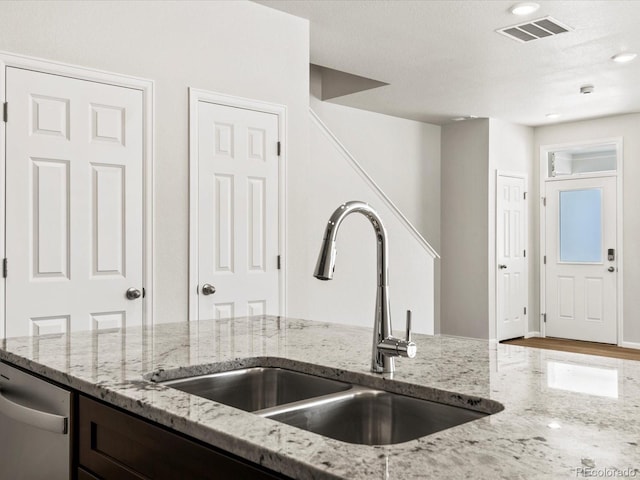 kitchen with stainless steel dishwasher, dark brown cabinets, light stone counters, visible vents, and a sink