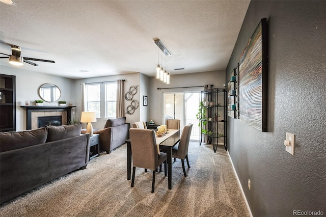 dining area featuring a tiled fireplace, ceiling fan, light carpet, and a textured ceiling