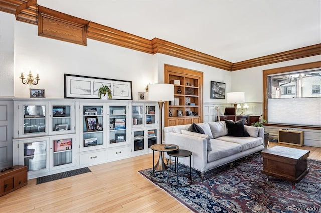 living room with built in shelves, ornamental molding, and light hardwood / wood-style floors